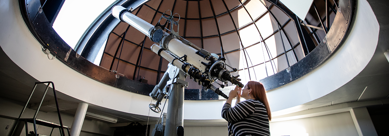 Woman looks through large telescope in an observatory.