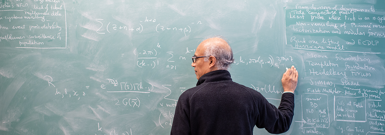 A proffessor stands at chalk board writing math equations.