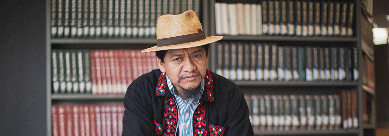 Prof Pedro Mateo Pedro looking at the camera in front of a book case.