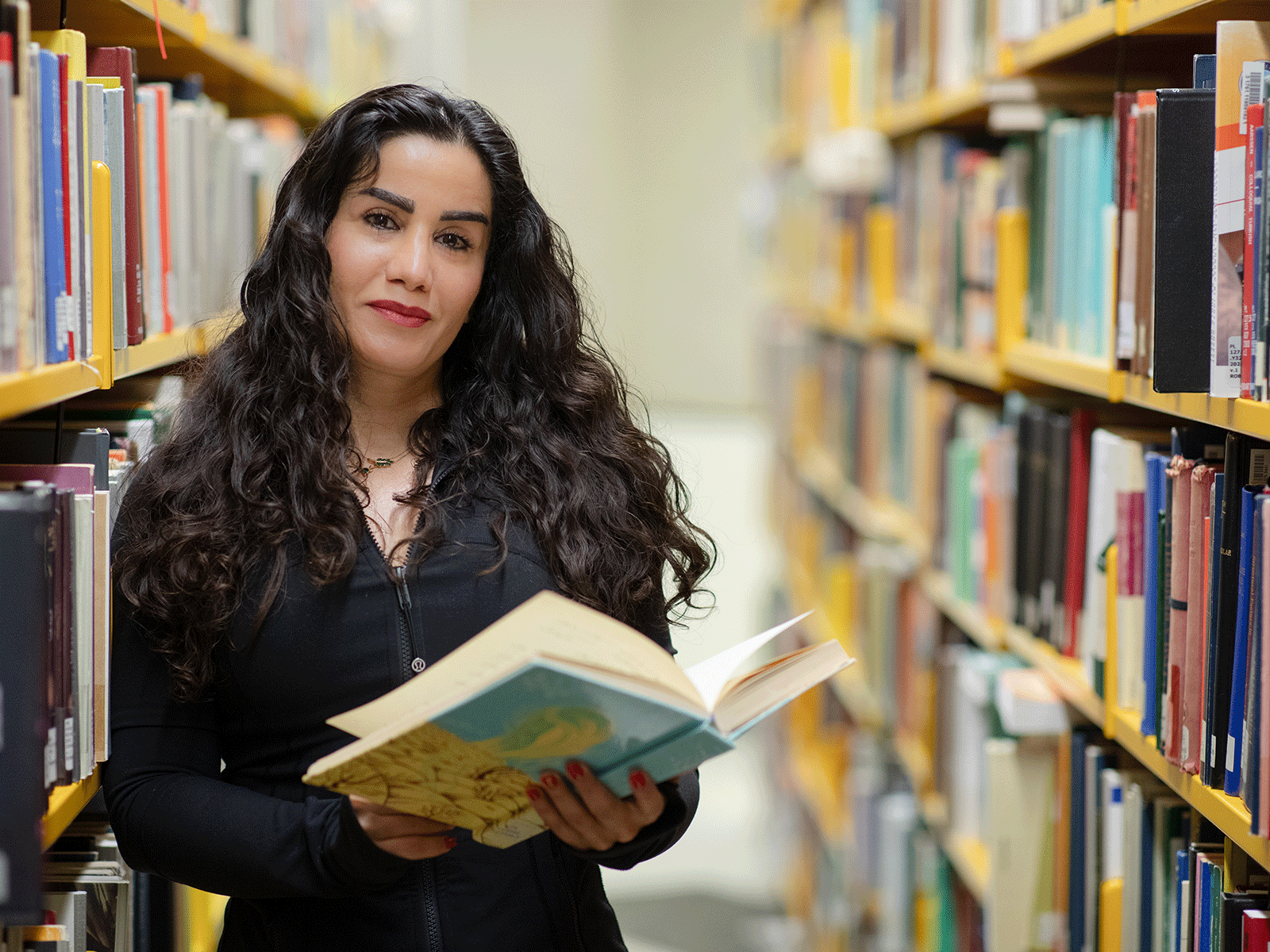 Headshot of Tayebeh Asadimofarah standing in a library stack, holding a book